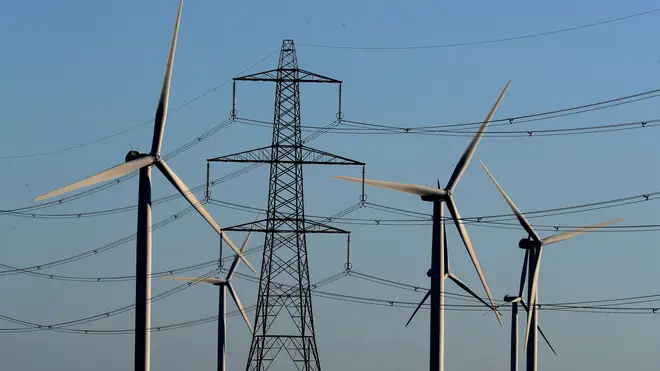 Wind turbines seen beyond an electricity pylon and wires